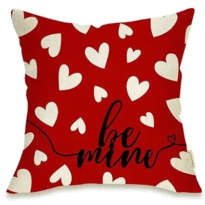 red pillow cover with white hearts placed throughout, in black cursive towards bottom right hand side says "Be mine"