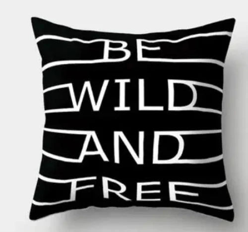 A black square throw pillow with the words "BE WILD AND FREE" in bold white letters.