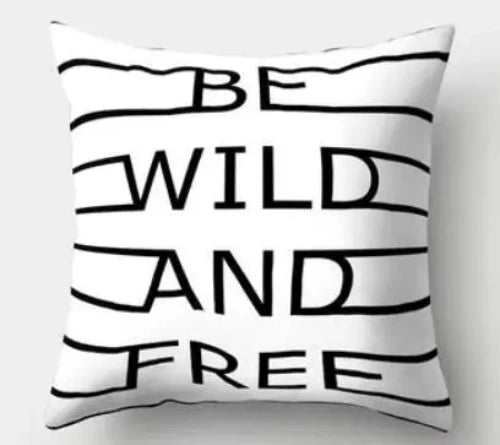 A white square throw pillow with the words "BE WILD AND FREE" in bold black letters.