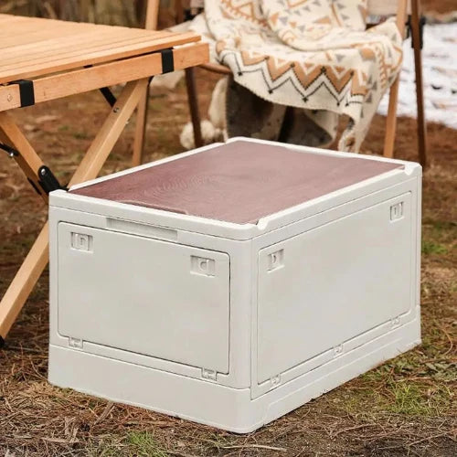 A white, foldable camping storage box is at a campsite near a picnic table