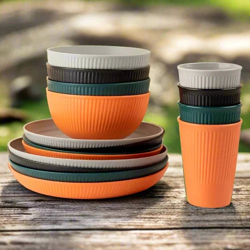 Four dinnerware sets of colored wheat straw are mixed up. All the cups are stacked to the right. The bowls are on the small plates which are on the large plates to the left. The colors are orange, dark green, black and grey.