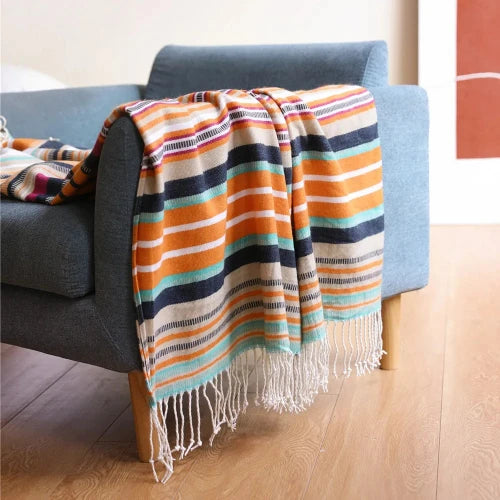 A brightly colored woven blanket with stripes of orange, blue, and white draped over the arm of a blue lounge chair.