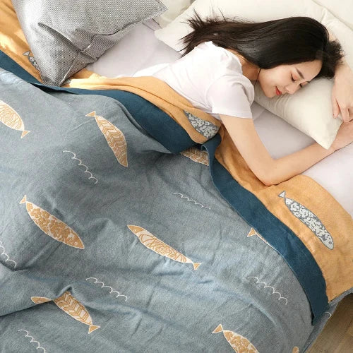 A person is sleeping and covered with a light blue comforter that has a repeating pattern of yellow fish and a blue border.