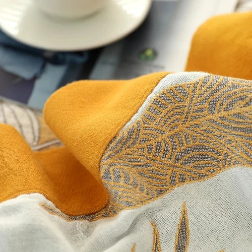 A close up of a white cotton blanket with blue and yellow shapes, and a yellow border.