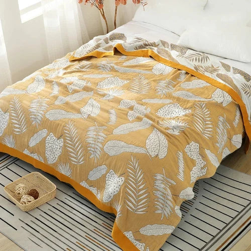 A yellow cotton gauze blanket with large white leaves and a yellow border is draped over a bed gives an aesthetic appeal.