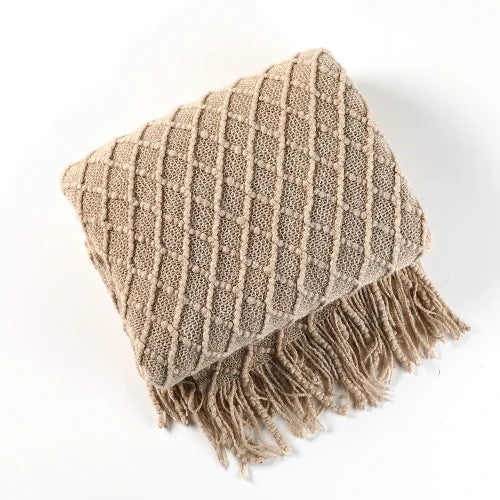 A khaki knit throw blanket with a textured pattern is folded and the tasseled ends are showing. 