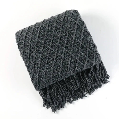 A dark blue knit throw blanket with a textured pattern is folded and the tasseled ends are showing.