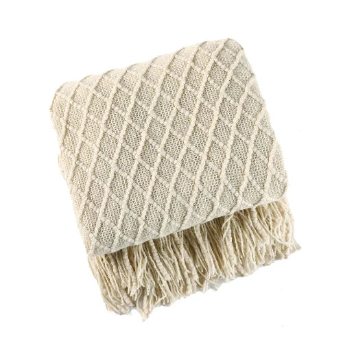 A cream colored knit throw blanket with a textured pattern is folded and the tasseled ends are showing.