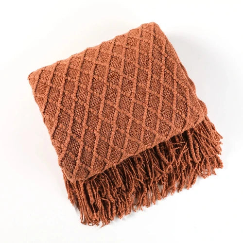 A brown knitted throw blanket with a textured pattern is folded and the tasseled ends are showing.