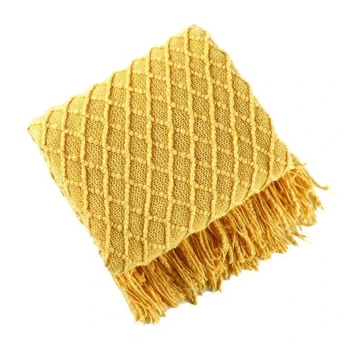 A yellow knit throw blanket with a textured pattern is folded and the tasseled ends are showing.