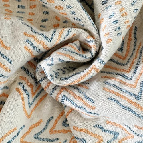 A close up of a cream-colored throw blanket with boho style shapes of muted orange and blue is twisted from the center.