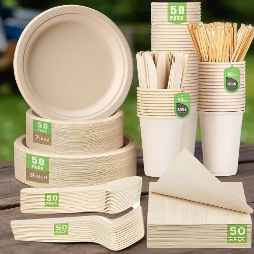 A set of cream-colored biodegradable disposable plates, cups, napkins and utensils are sitting on a wooden table to be used for a picnic.