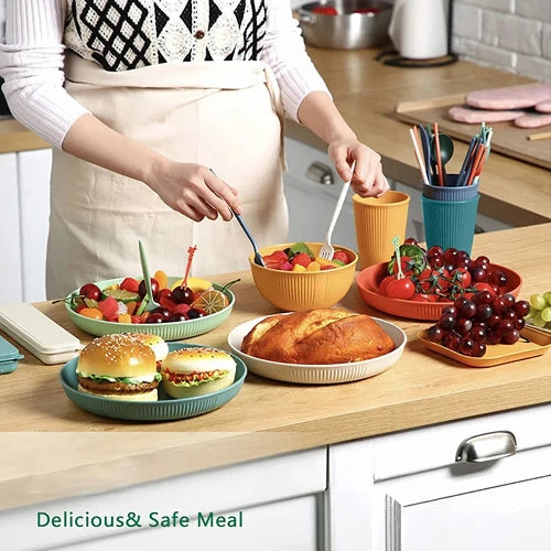 A counter with colorful wheat straw dinnerware including plates, bowls, and cups that are filled with various foods like fruit, bread, and sandwiches.