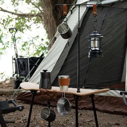 A wooden skateboard table with a lantern, cups, and bowls hanging from it is at a campsite in front of a tent. 