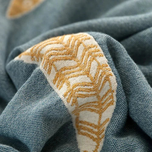 A close up of a light blue throw blanket with a yellow stitched pattern.