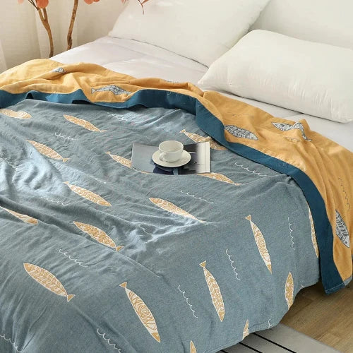 A light blue comforter with a repeating pattern of yellow fish and a blue border is covering a bed. A teacup and saucer sit on the bed.